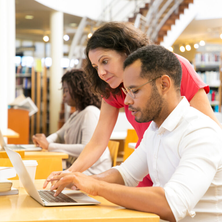 Side view of colleagues working with laptop at library. Two students working with laptops together. Education concept